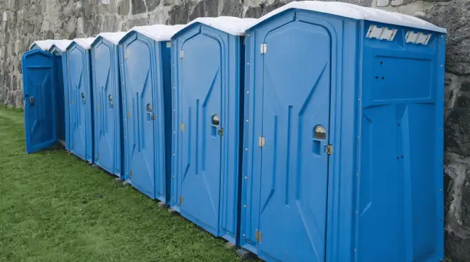 Row of blue portable toilets lined up on grass against a stone wall for event sanitation in Allentown, PA