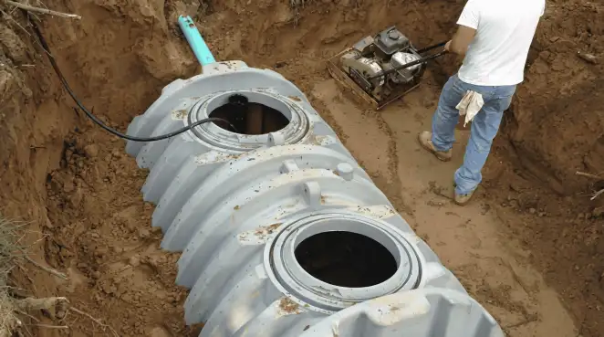 Septic tank installation showing a technician compacting soil around a new poly septic tank in an excavation pit in Allentown, PA